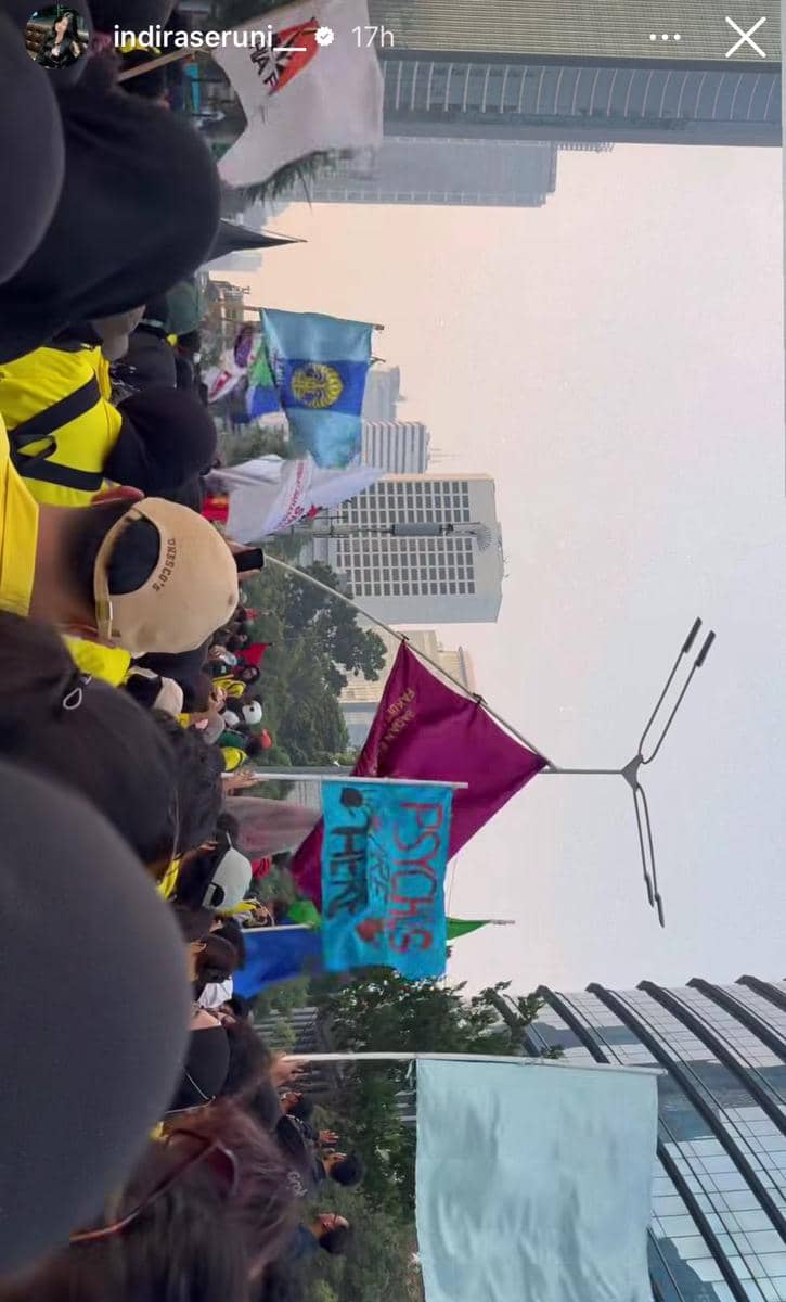 Kerumunan mahasiswa mengenakan jaket kuning membawa berbagai bendera dan spanduk saat demonstrasi di area gedung tinggi Jakarta.