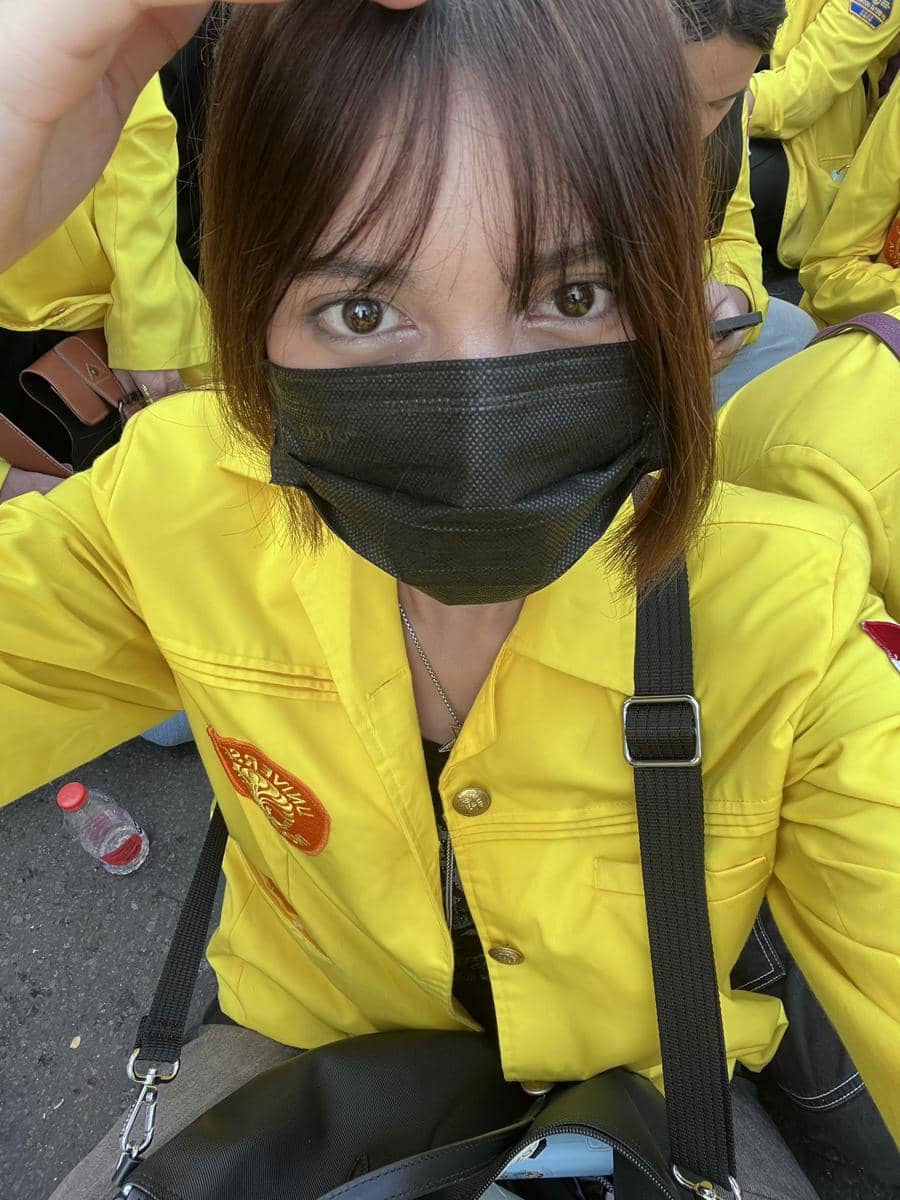 Seorang mahasiswa mengenakan jaket almamater kuning dan masker hitam saat mengikuti aksi bersama rekan-rekannya di luar ruangan.