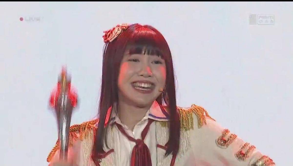 Seorang anggota JKT48 tersenyum di atas panggung saat penampilan live JKT48 Request Hour 2026 dengan pencahayaan merah.