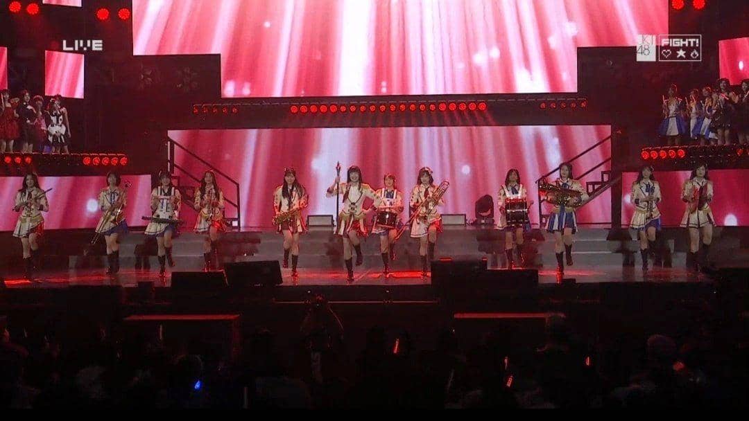 Penampilan grup idola JKT48 di panggung JKT48 Request Hour 2026 dengan pencahayaan merah dan latar layar besar.