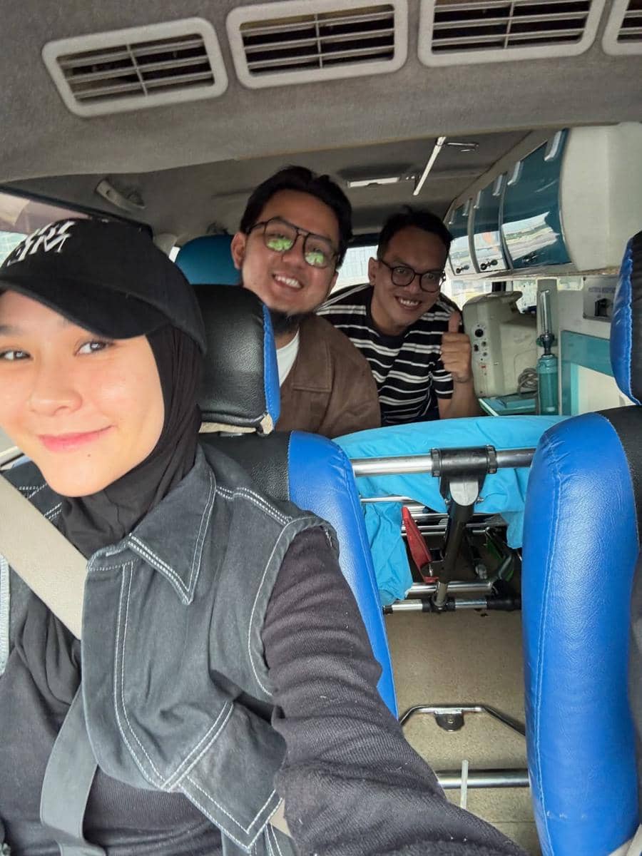 Seorang perempuan berhijab berfoto selfie di dalam mobil bersama dua pria yang tersenyum di kursi belakang.