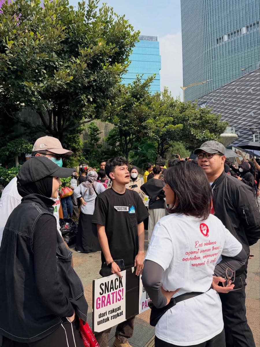 Sejumlah relawan berbincang di tengah aksi demo mahasiswa di area perkotaan dengan gedung tinggi di latar belakang.