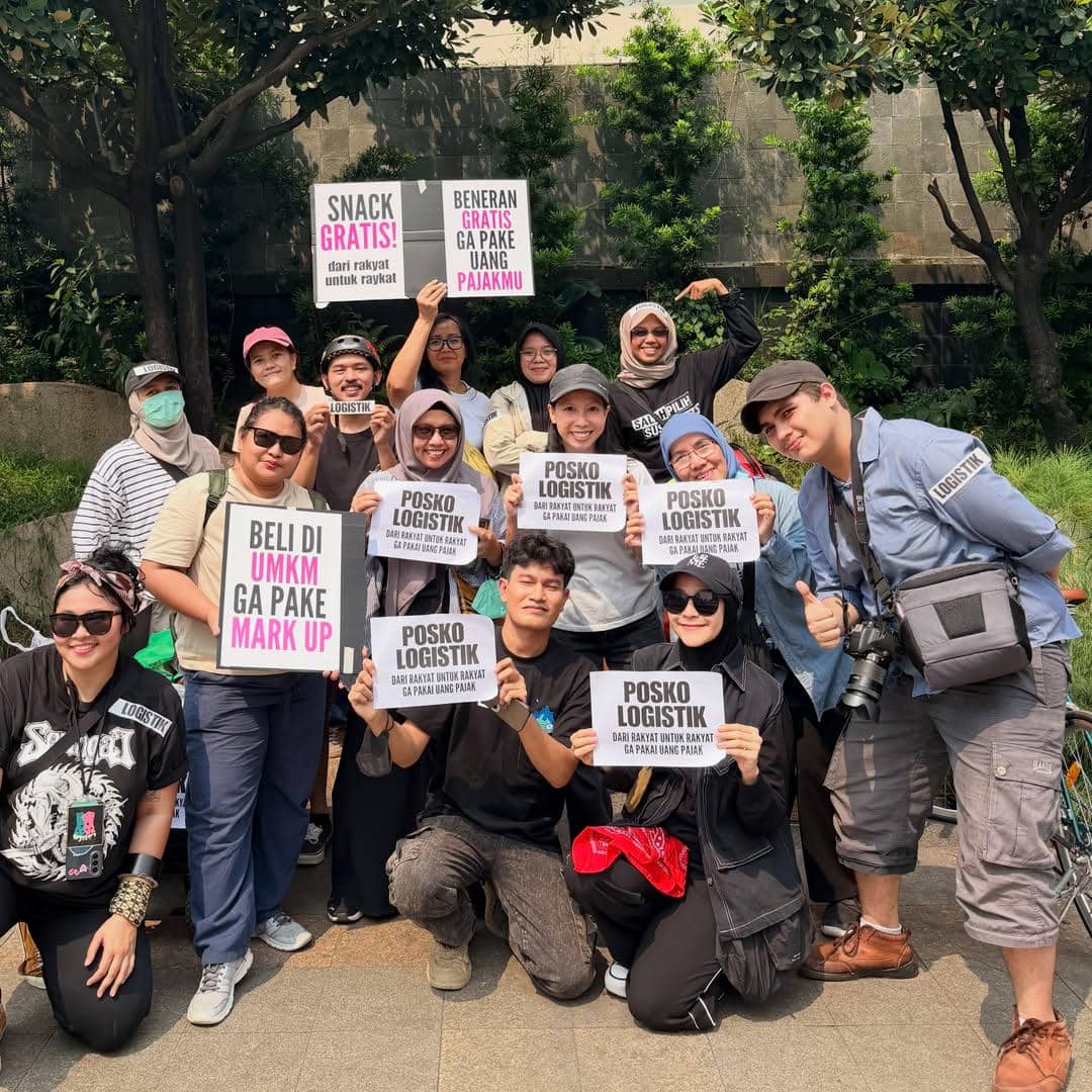 Sekelompok relawan memegang poster bertuliskan dukungan logistik dan pesan solidaritas dalam aksi demo mahasiswa di area terbuka.
