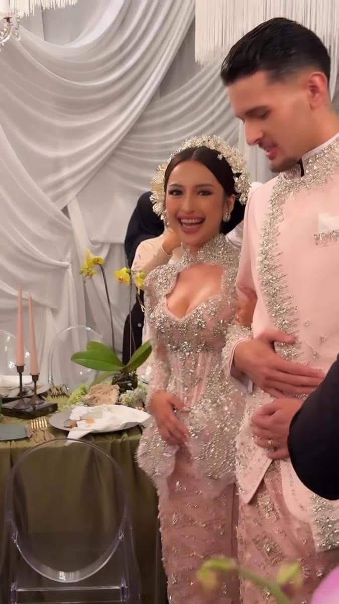 Pasangan mengenakan busana adat modern berwarna pink berhias payet di acara makan malam pernikahan dengan dekorasi elegan bernuansa putih.