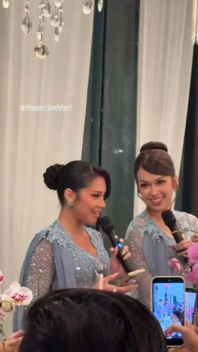 Dua wanita mengenakan gaun biru berhias payet sedang berbicara dengan mikrofon di acara makan malam pernikahan yang elegan.