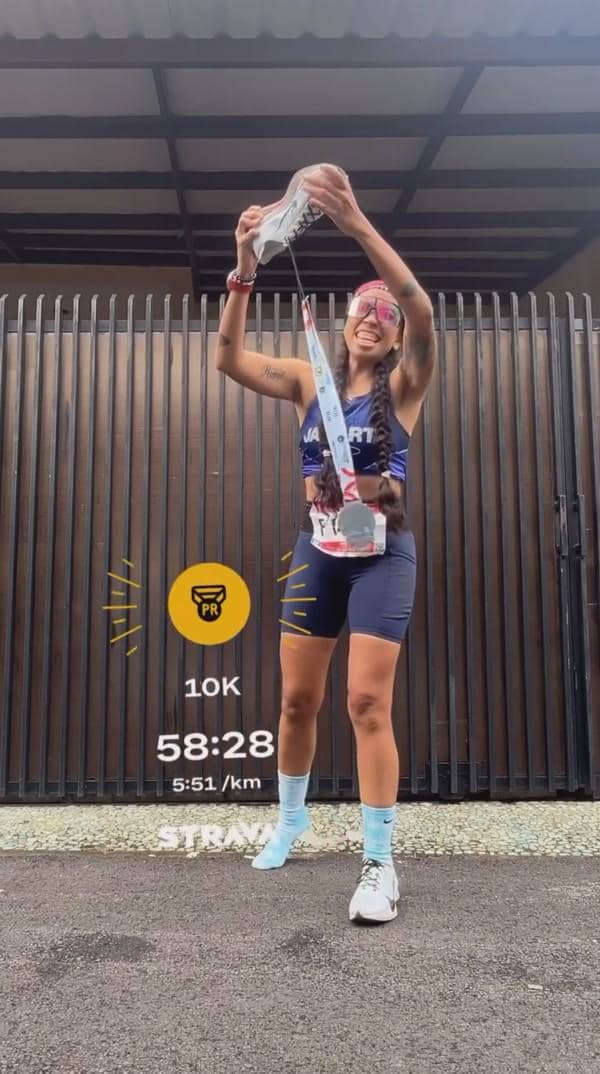 Seorang pelari perempuan tersenyum sambil mengangkat sepatu dan medali setelah menyelesaikan lomba lari 10K Jakarta International Marathon 2026.