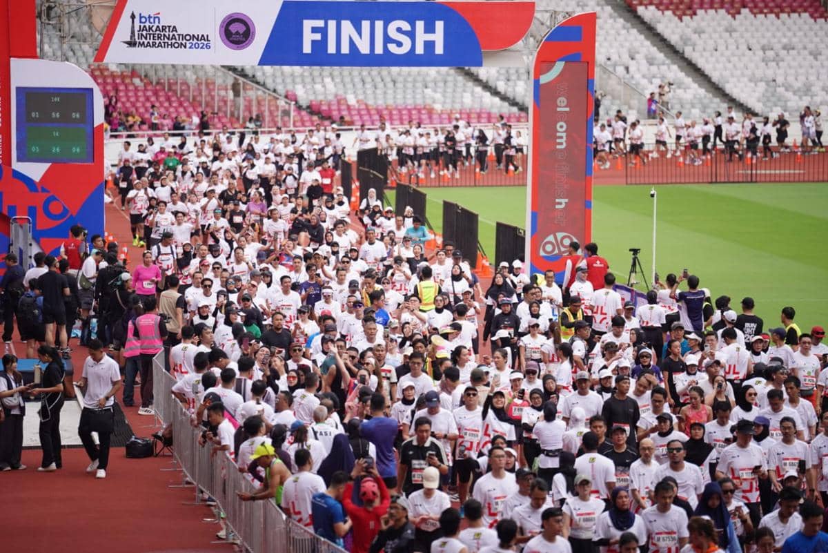 Ratusan peserta marathon mengenakan kaus putih melintasi garis finis di Stadion Gelora Bung Karno pada BTN Jakarta International Marathon 2026.