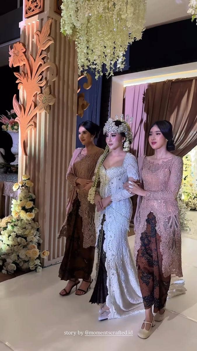 Pengantin wanita mengenakan kebaya putih dan siger Sunda berjalan di pelaminan didampingi dua perempuan berkebaya cokelat.