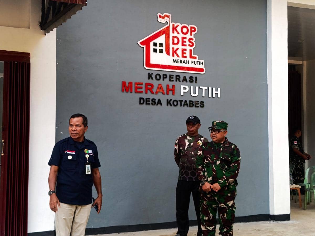 Beberapa pria, termasuk anggota TNI, berdiri di depan gedung bertuliskan Koperasi Merah Putih Desa Kotabes di Kupang, NTT.