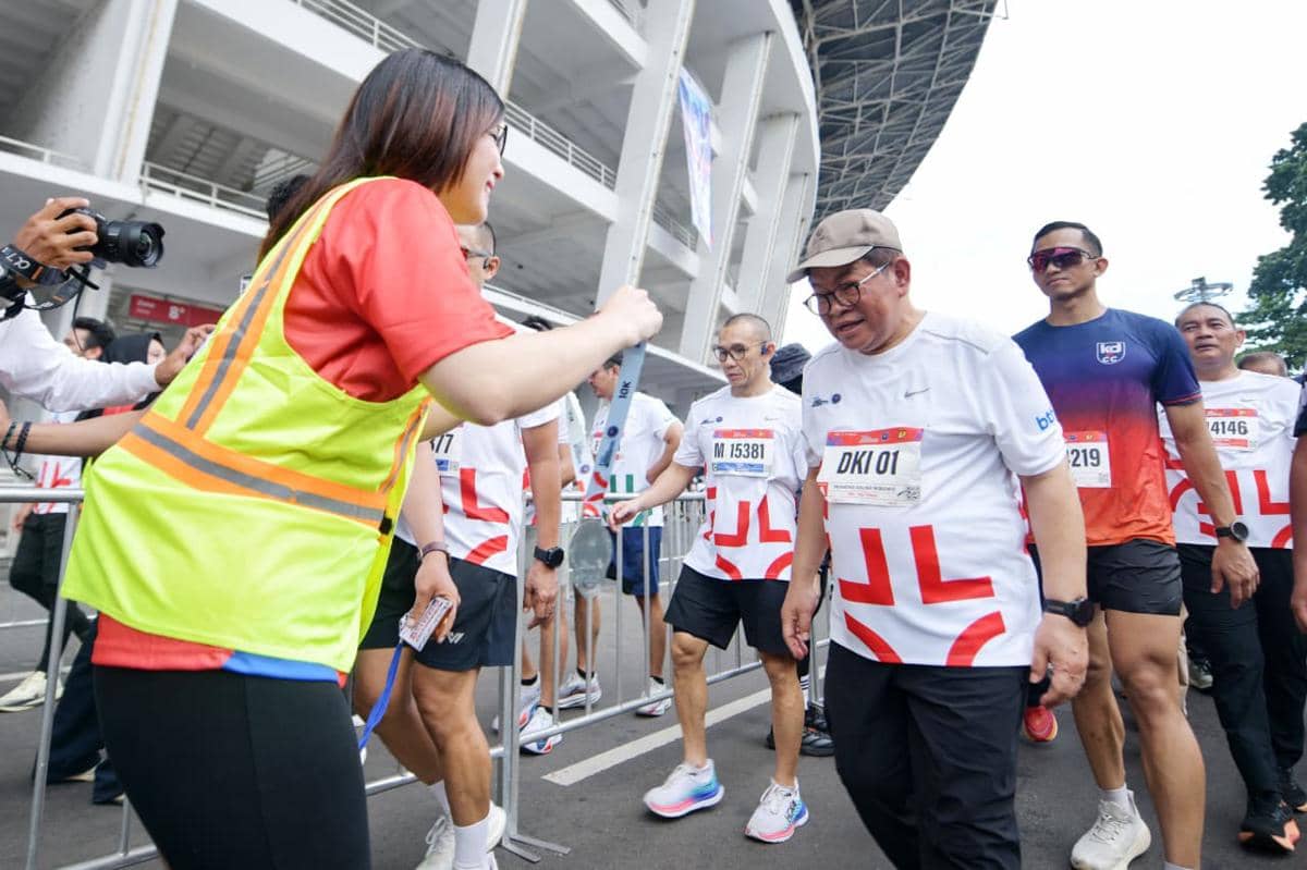 Peserta BTN JAKIM 2026 mengenakan kaus bernomor dada berjalan di area luar stadion sambil menerima medali dari panitia acara.