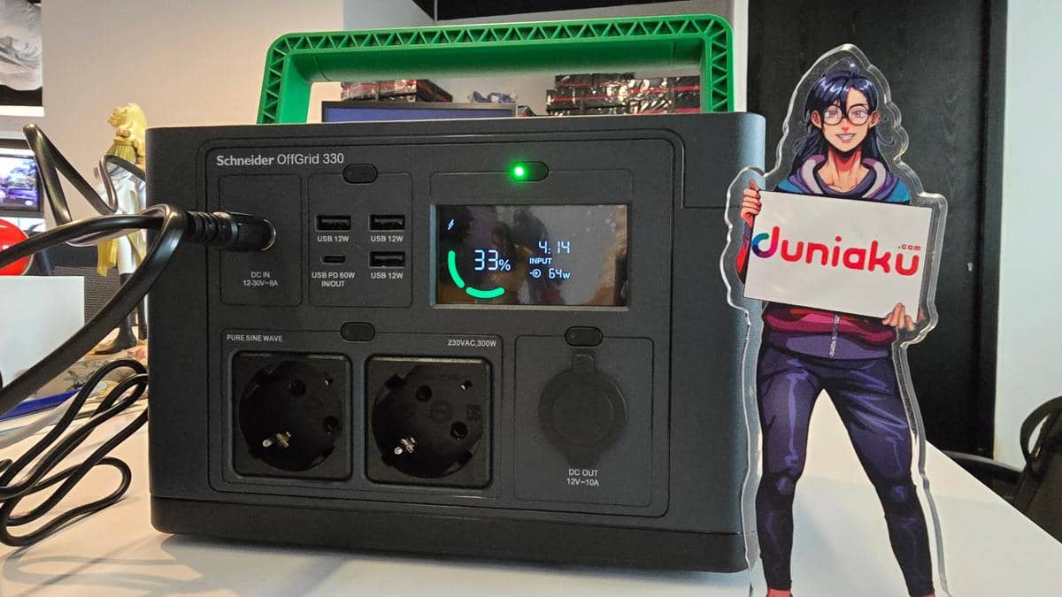 Stasiun daya portabel Schneider OffGrid 330 dengan layar indikator daya menyala di meja, berdampingan dengan figur kartun memegang papan bertuliskan Duniaku.