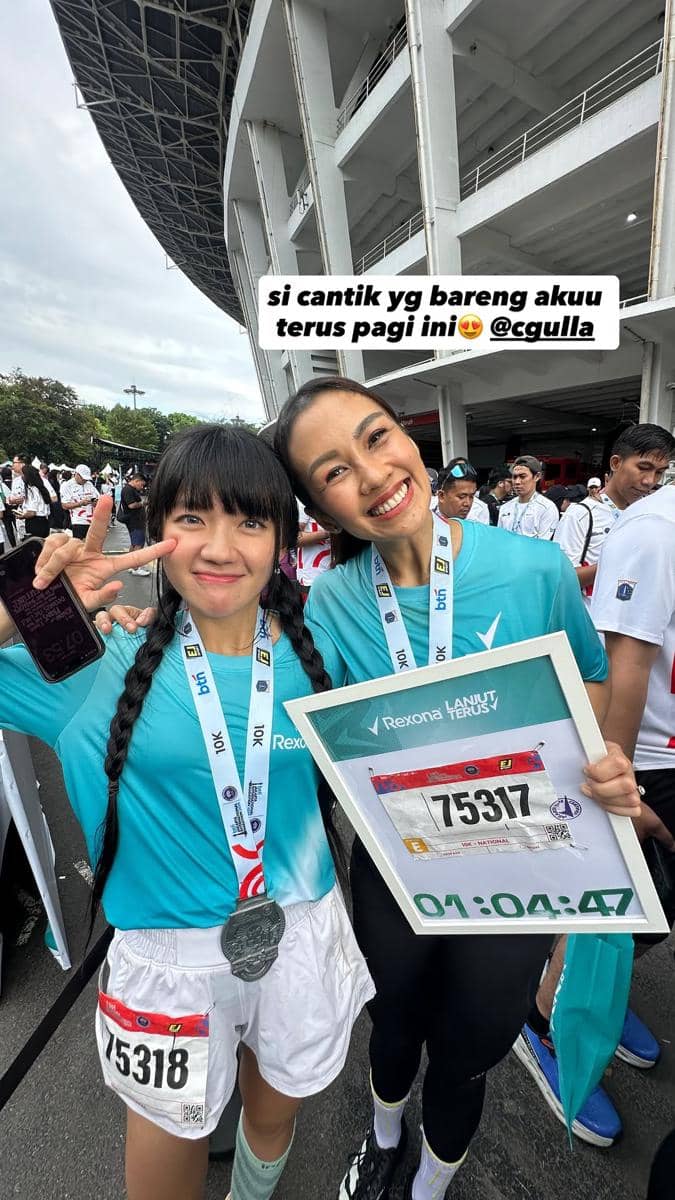 Dua pelari perempuan mengenakan kaus biru muda dan medali finisher berpose ceria setelah menyelesaikan Jakarta International Marathon 2026.