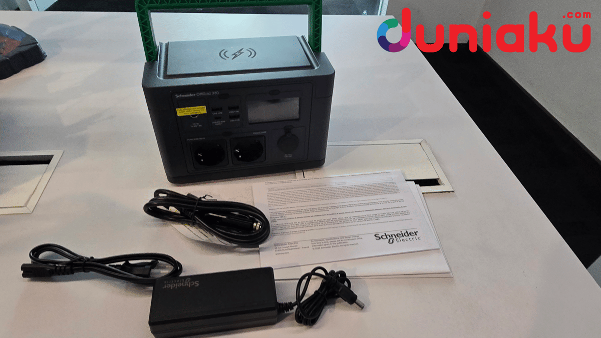 Stasiun daya portabel Schneider Offgrid 330 berwarna hitam dengan pegangan hijau, disertai kabel dan adaptor di atas meja.