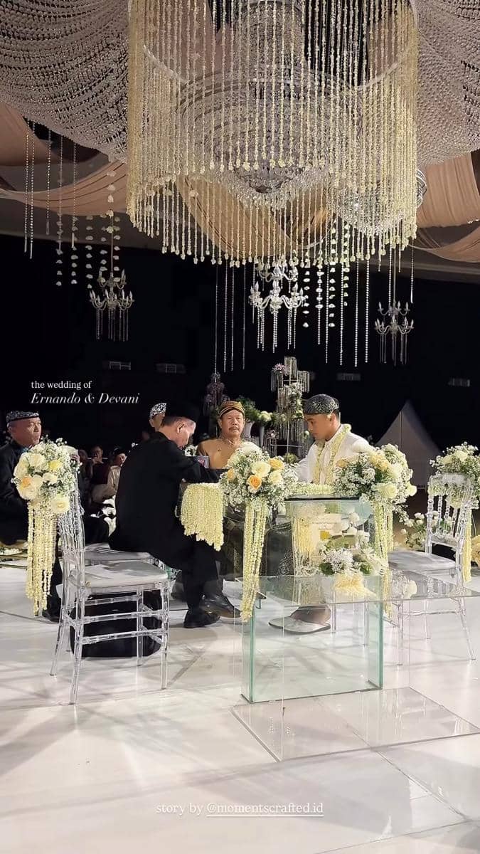 Suasana akad nikah Ernando Ari dan Devina Audri dengan dekorasi mewah bernuansa putih dan emas di bawah lampu gantung kristal.