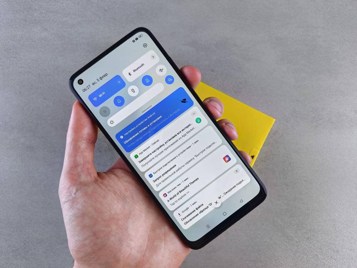 Seseorang memegang ponsel pintar yang menampilkan layar notifikasi dan pengaturan cepat seperti Wi-Fi serta Bluetooth aktif.
