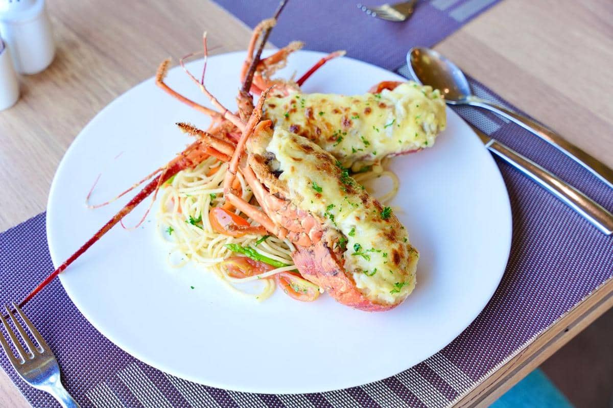 Lobster thermidor dengan saus keju panggang disajikan di atas piring bersama pasta dan sayuran di meja makan.