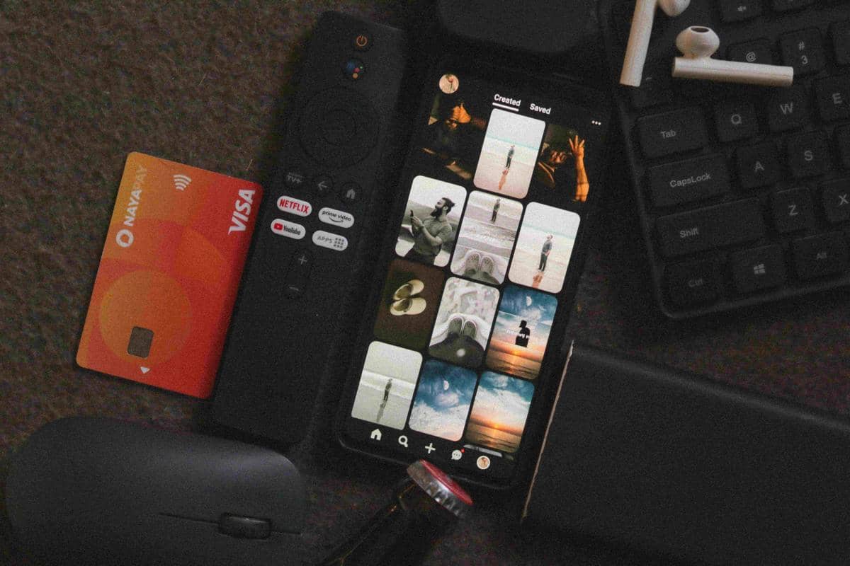Kartu debit berwarna oranye, remote TV dengan tombol layanan streaming, dan ponsel menampilkan galeri foto di atas meja.
