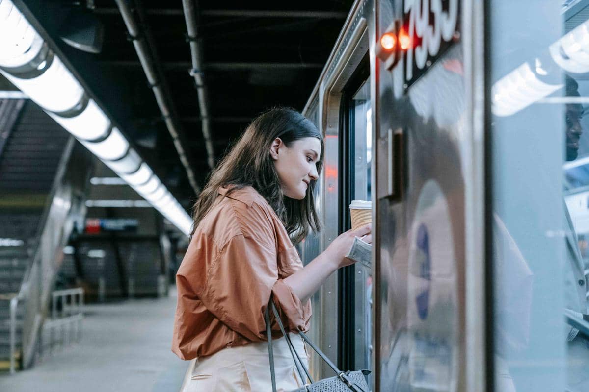 Seorang wanita berdiri di stasiun bawah tanah sambil membeli kopi dari jendela penjual dengan suasana modern dan pencahayaan neon.
