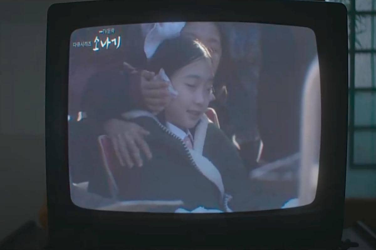 Adegan dari drama My Royal Nemesis yang menampilkan seorang gadis muda berseragam sekolah sedang duduk dan tersenyum di layar televisi.