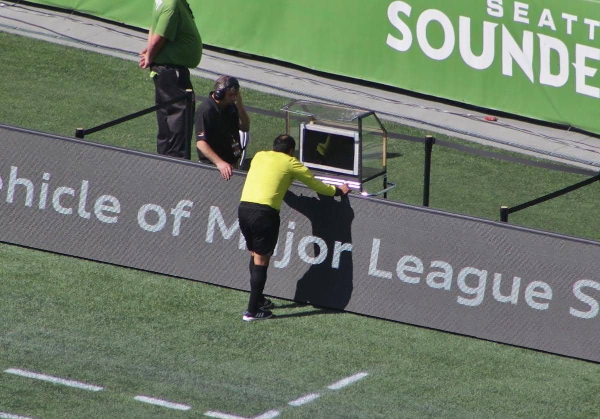 Wasit utama berseragam kuning sedang melihat layar monitor VAR di pinggir lapangan sepak bola didampingi petugas operator