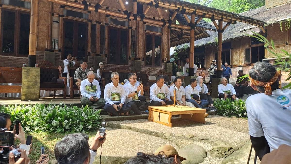 Sekelompok orang duduk bersama di depan bangunan bambu tradisional, mengikuti acara bertema konservasi di ruang terbuka hijau.