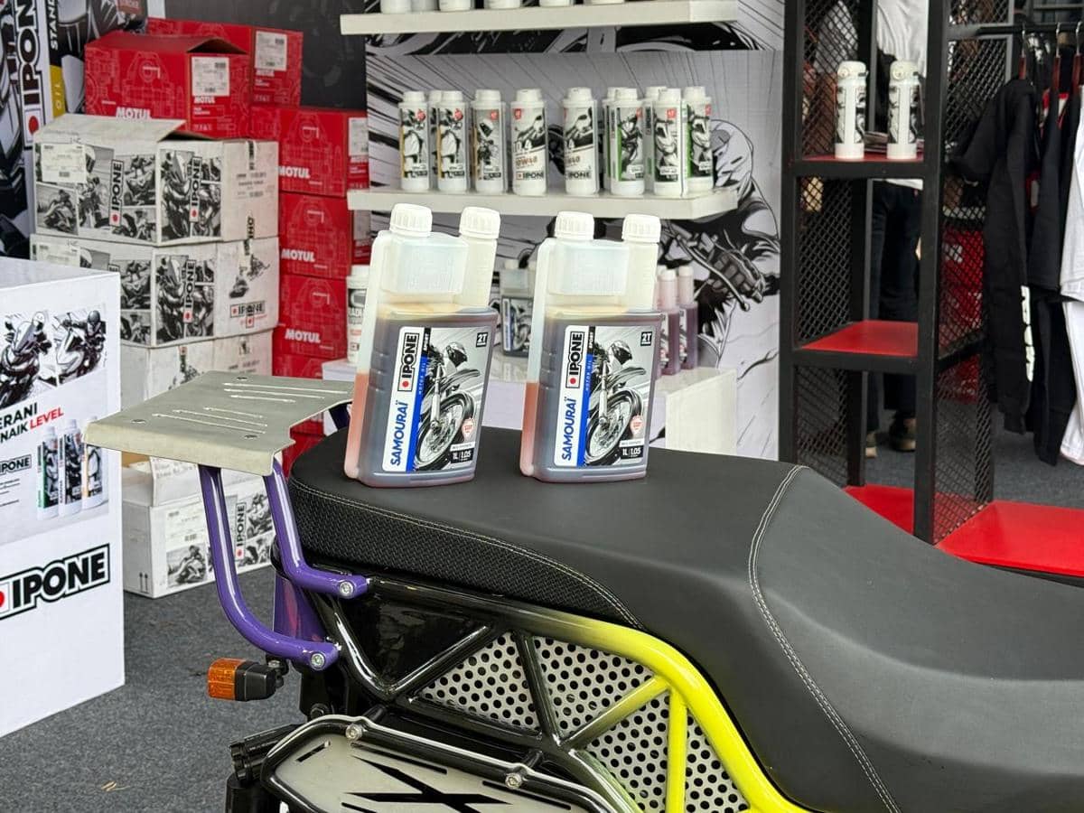 Dua botol oli Ipone Samouraï 2T diletakkan di atas jok motor dengan latar belakang rak berisi produk pelumas lainnya.