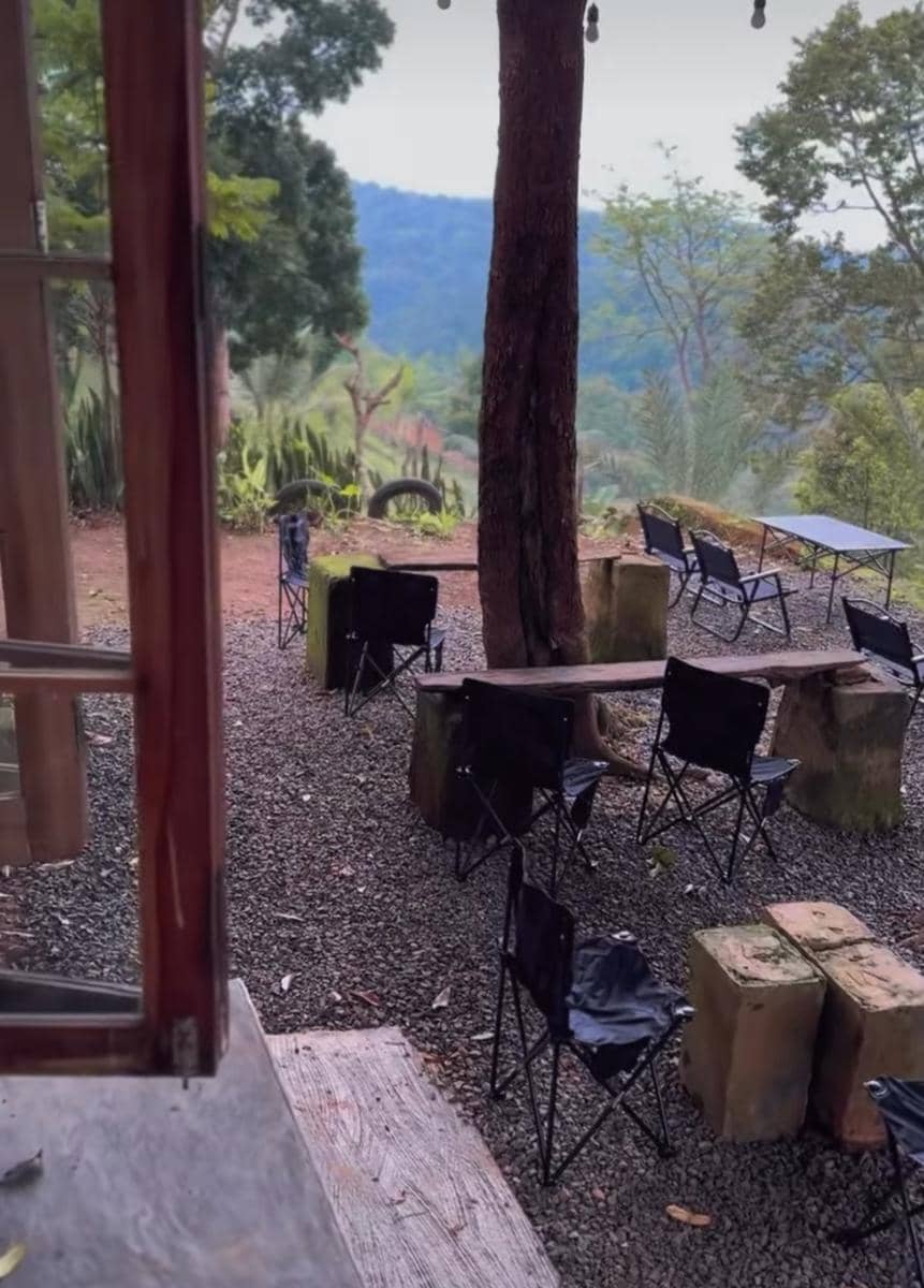 Area duduk outdoor Ramen Meledak Kaizen di Kemiling Bandar Lampung dengan kursi lipat hitam dan pemandangan pepohonan hijau.