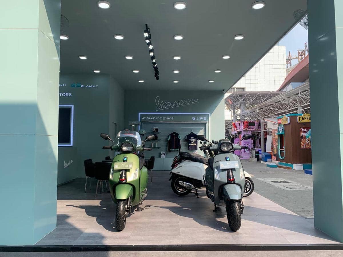 Dua skuter Vespa dipamerkan di booth berwarna hijau dengan pencahayaan modern di area pameran JFK 2026.