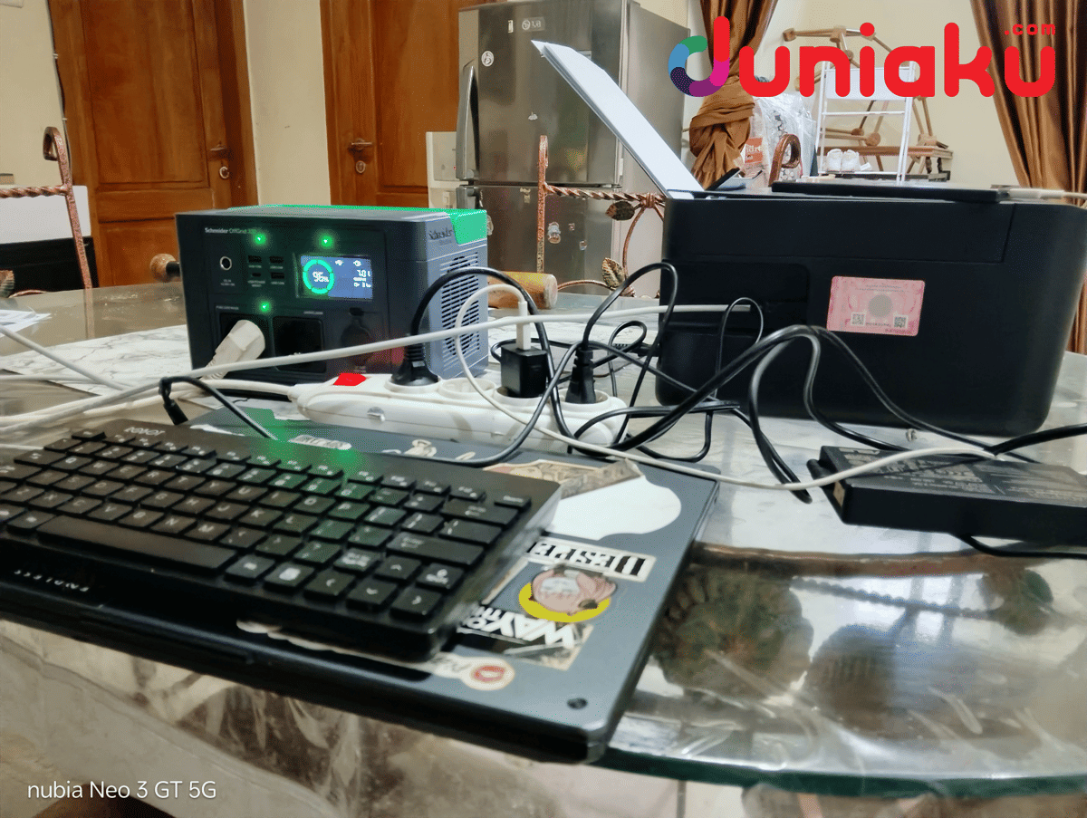 Schneider Portable Power Station digunakan untuk mengisi daya berbagai perangkat elektronik di atas meja, termasuk printer dan keyboard.