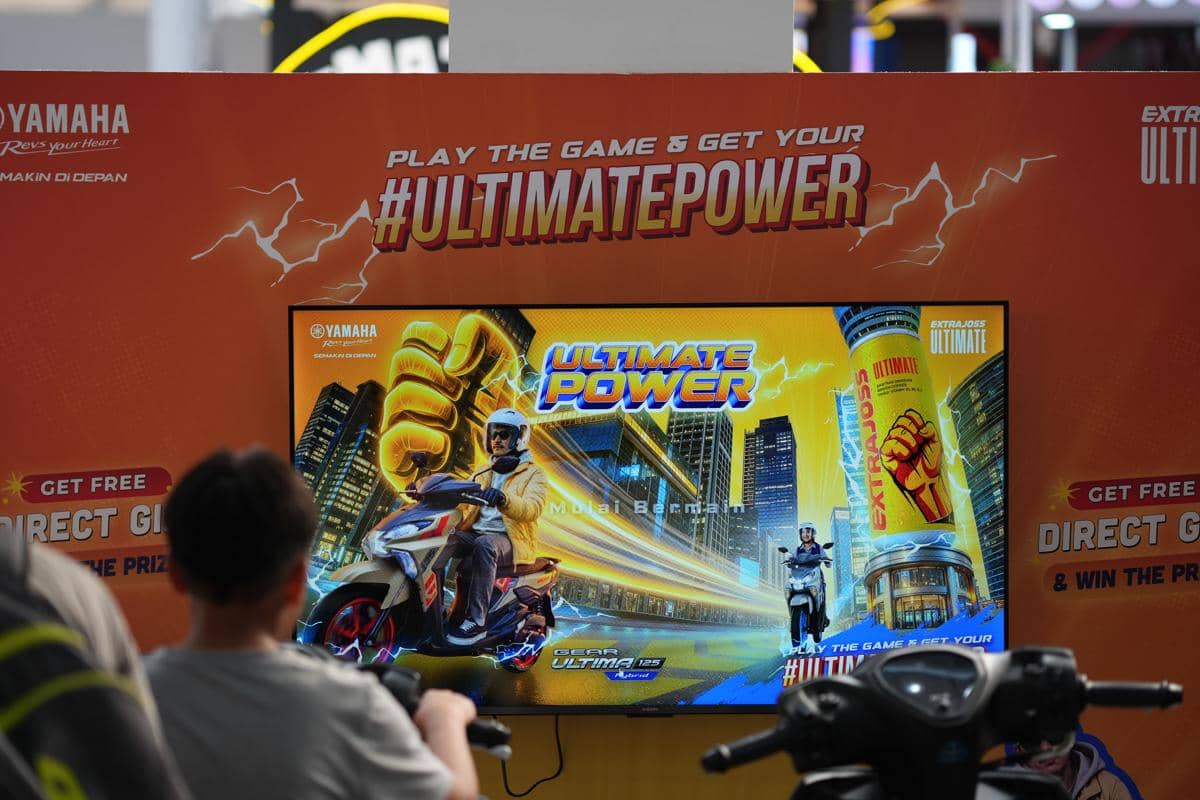 Pengunjung mencoba permainan bertema Ultimate Power di stan Yamaha dengan layar besar menampilkan promosi motor dan minuman energi.