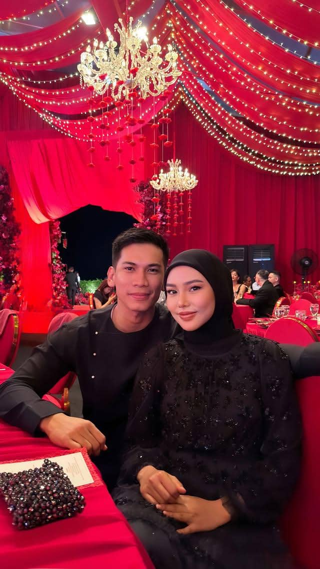 Sepasang tamu duduk di meja dengan dekorasi merah dan lampu gantung mewah di resepsi pernikahan Jennifer Coppen dan Justin.
