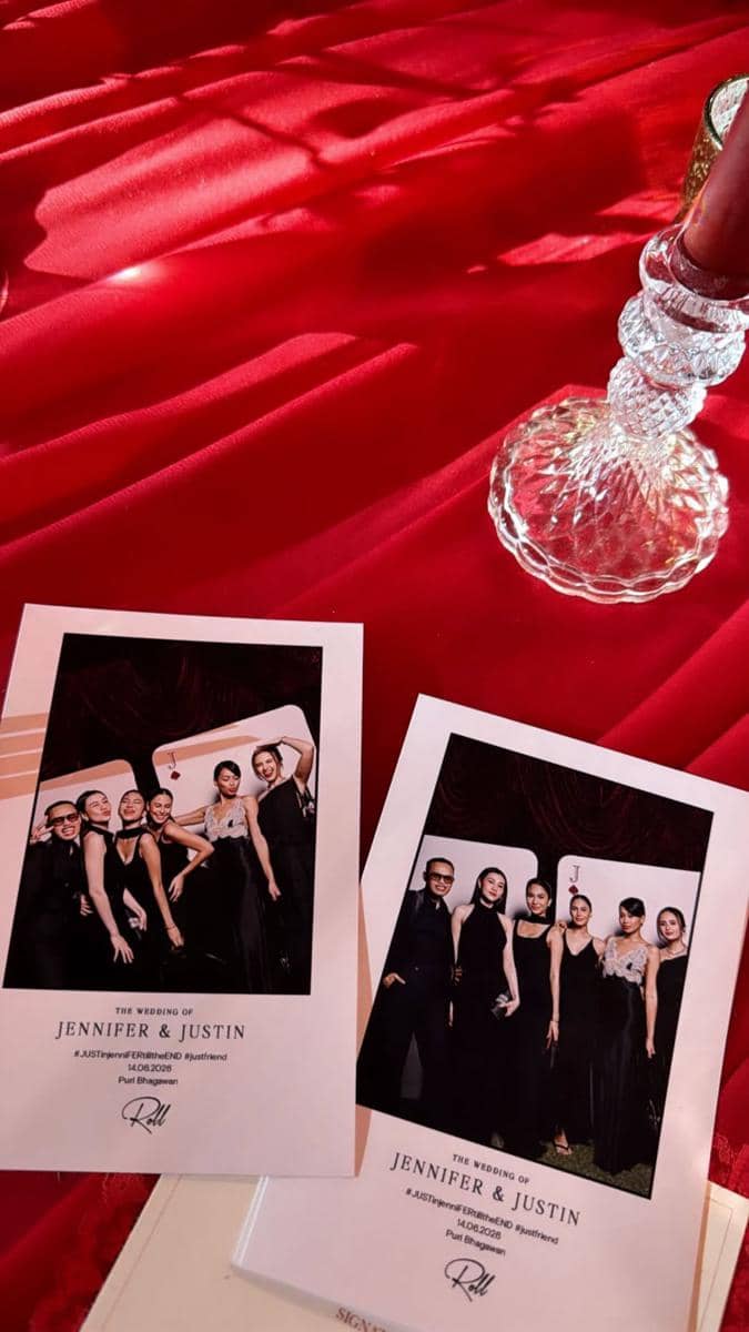 Dua kartu foto tamu dari resepsi pernikahan Jennifer dan Justin diletakkan di atas kain merah dengan hiasan lilin kaca di sampingnya.