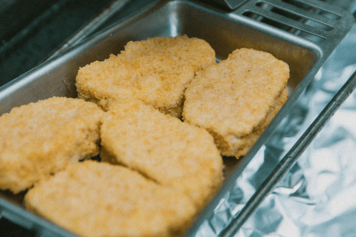 Potongan daging ayam berlapis tepung roti disusun di wadah logam sebagai persiapan membuat chicken katsu renyah.