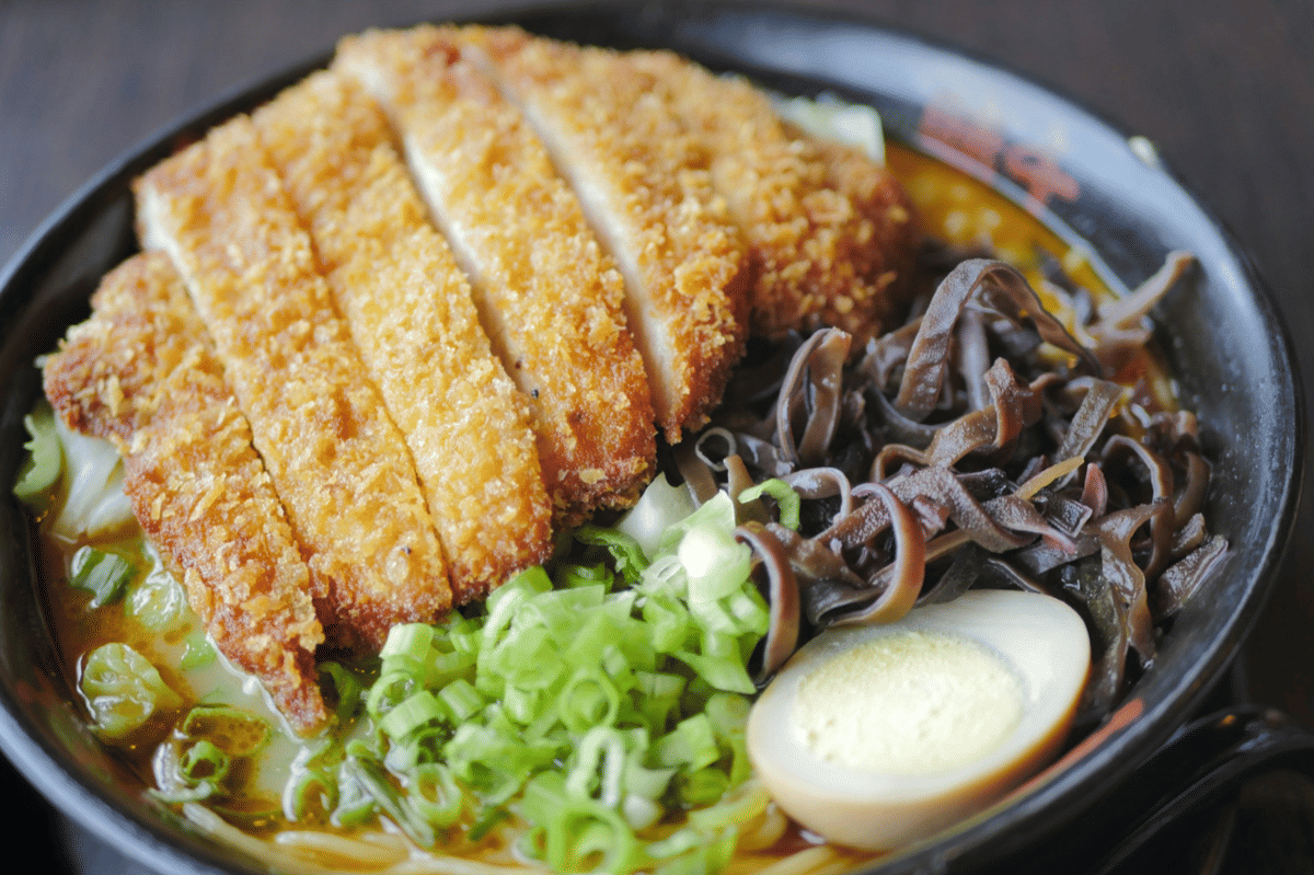 Semangkuk ramen dengan topping chicken katsu renyah, telur rebus setengah, jamur, dan irisan daun bawang segar.