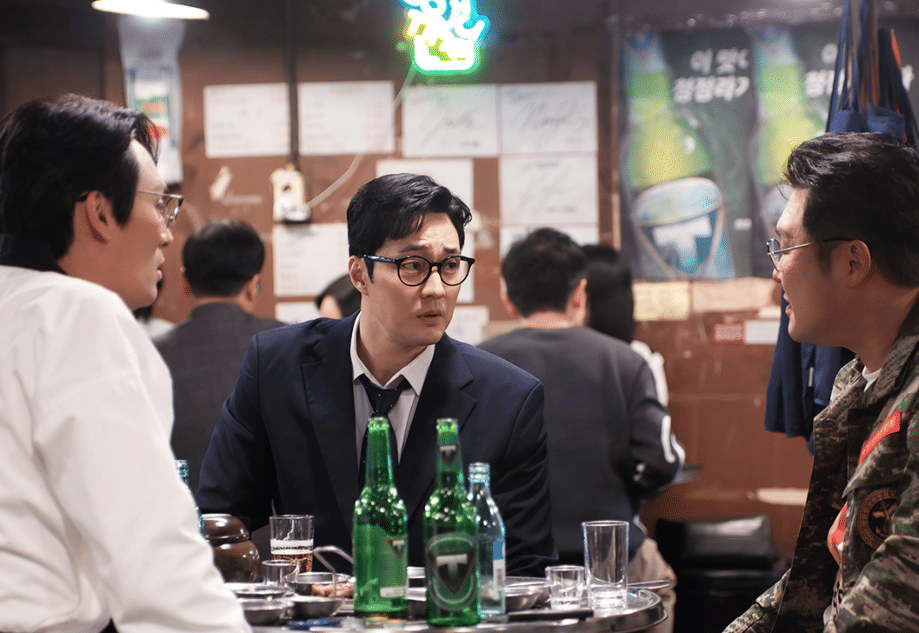 Tiga pria sedang berbincang serius di meja restoran dengan botol minuman di depan mereka dalam adegan drama Korea Agent Kim Reactivated.