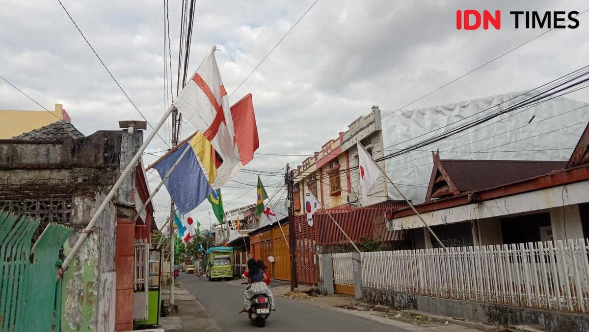 Deretan bendera negara peserta Piala Dunia 2026 terpasang di sepanjang Jalan Titang, Makassar, dengan langit berawan di atasnya.