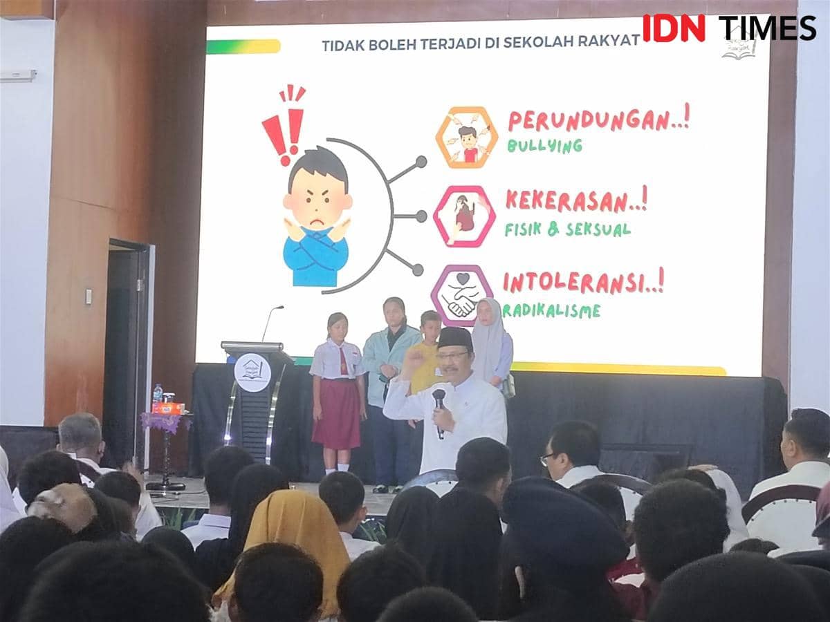 Seorang pejabat berbicara di depan peserta open house Sekolah Rakyat dengan latar layar berisi pesan anti perundungan, kekerasan, dan intoleransi.