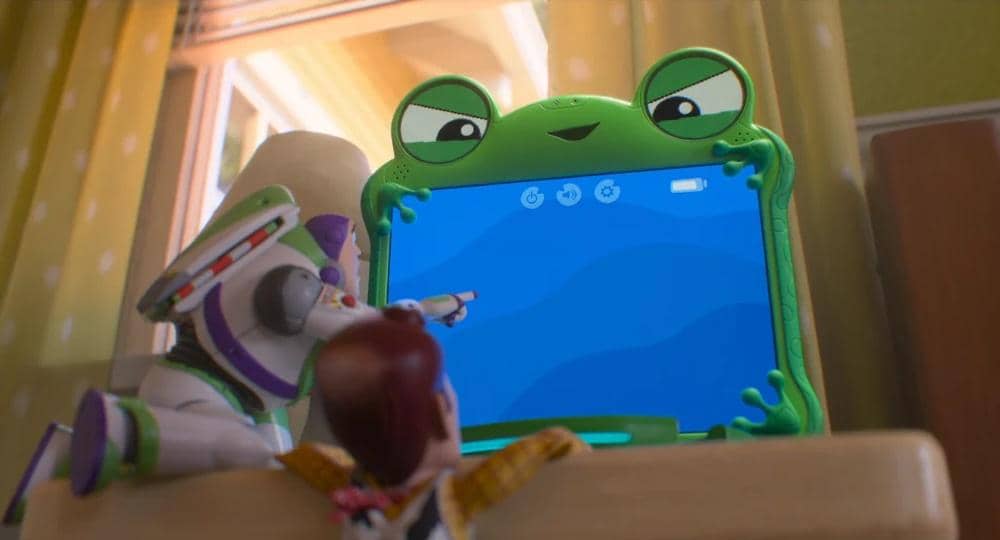 Buzz Lightyear dan Woody melihat layar tablet berbentuk katak di atas meja dalam adegan film animasi Toy Story 5.