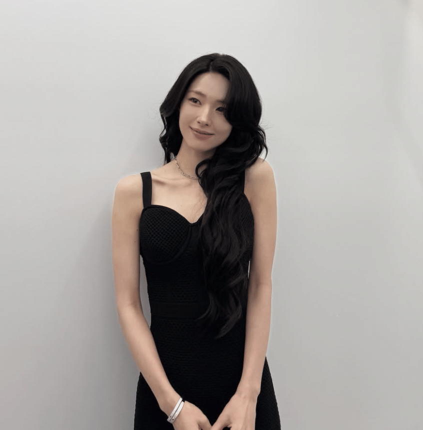 Aktris Ha Young mengenakan gaun hitam tanpa lengan berdiri di depan dinding berwarna abu muda.