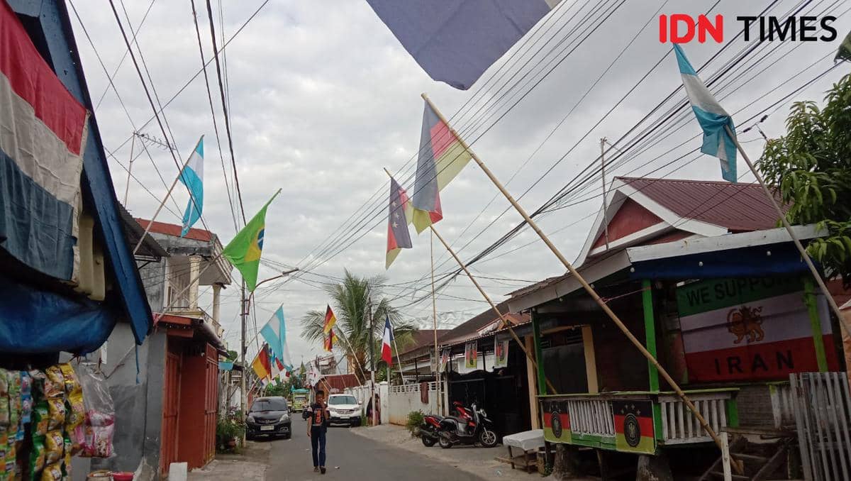 Deretan bendera negara peserta Piala Dunia 2026 berkibar di sepanjang Jalan Titang, Makassar, dengan suasana permukiman warga yang ramai.