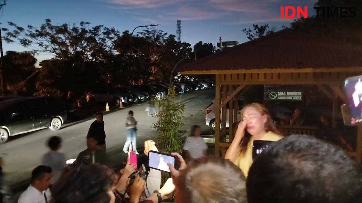 Seorang pendukung menangis di luar Pengadilan Negeri Manado setelah sidang praperadilan pada malam hari dengan kerumunan orang di sekitarnya.