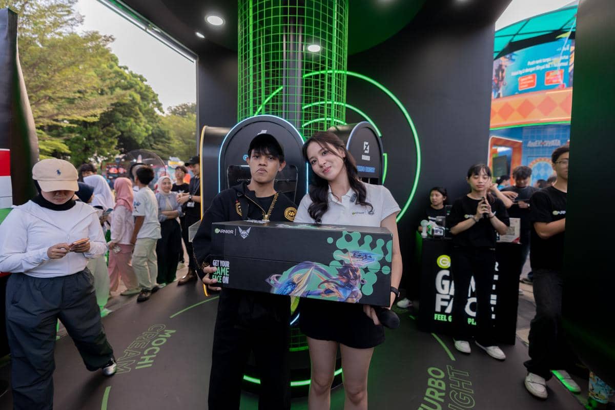 Dua pengunjung berpose di booth pop up Garnier Game Face saat grand playoffs MPL Indonesia S17 dengan latar desain hijau futuristik.
