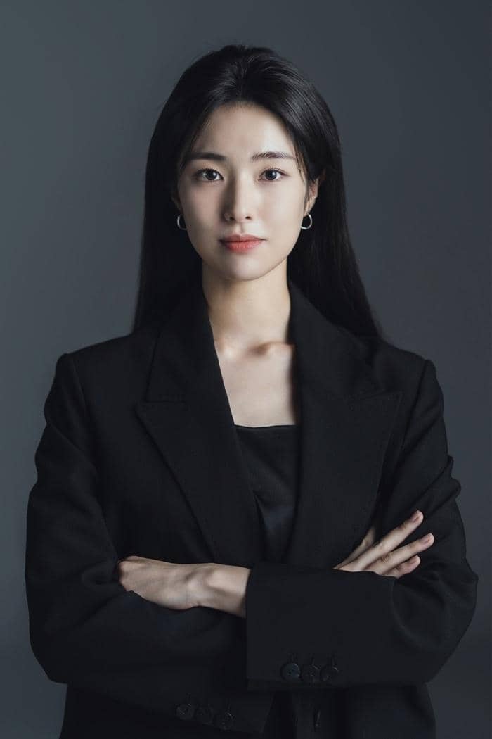 Ahn Ha Young mengenakan setelan jas hitam dengan tangan terlipat, berpose di depan latar abu-abu gelap.