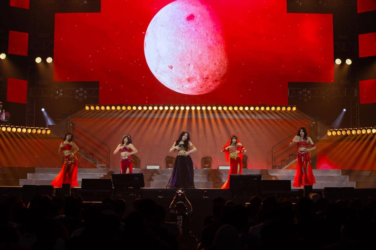 Lima penampil menari di atas panggung dengan latar bulan merah besar dan pencahayaan dramatis dalam konser musik JKT48.