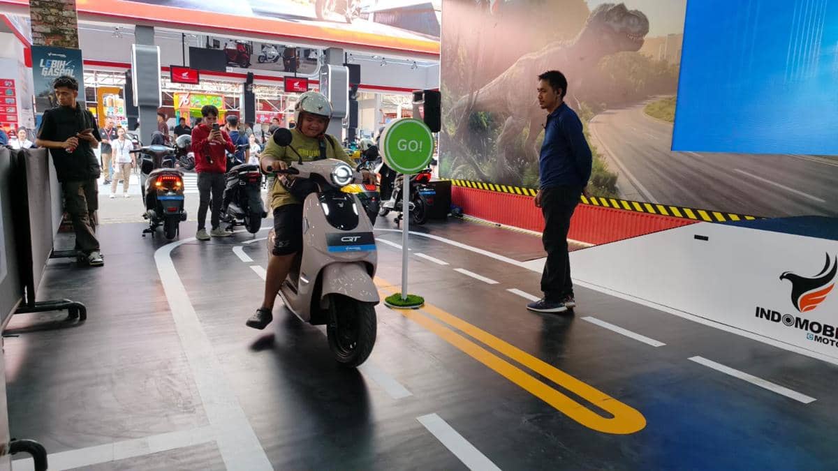 Pengunjung mencoba motor listrik di area test drive dalam ruangan dengan jalur simulasi dan pengawasan instruktur.