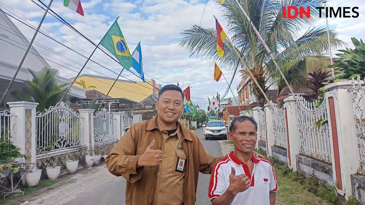 Dua pria berdiri di jalan perumahan di Makassar dengan latar bendera berbagai negara yang dipasang di sepanjang jalan.