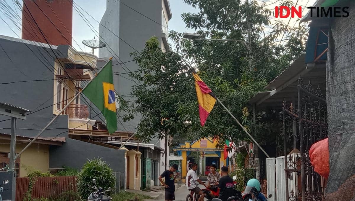 Bendera negara peserta Piala Dunia 2026 terpasang di sepanjang Jalan Titang, Makassar, dengan beberapa warga berbincang di tepi jalan.