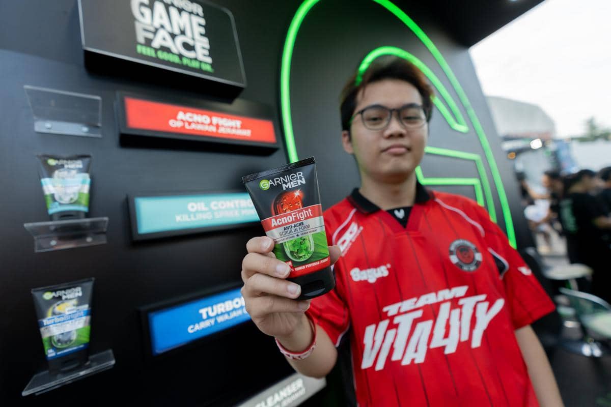 Seorang pengunjung mengenakan jersey merah memegang produk Garnier Men AcnoFight di booth #GarnierGameFace pada grand playoffs MPL Indonesia S17.