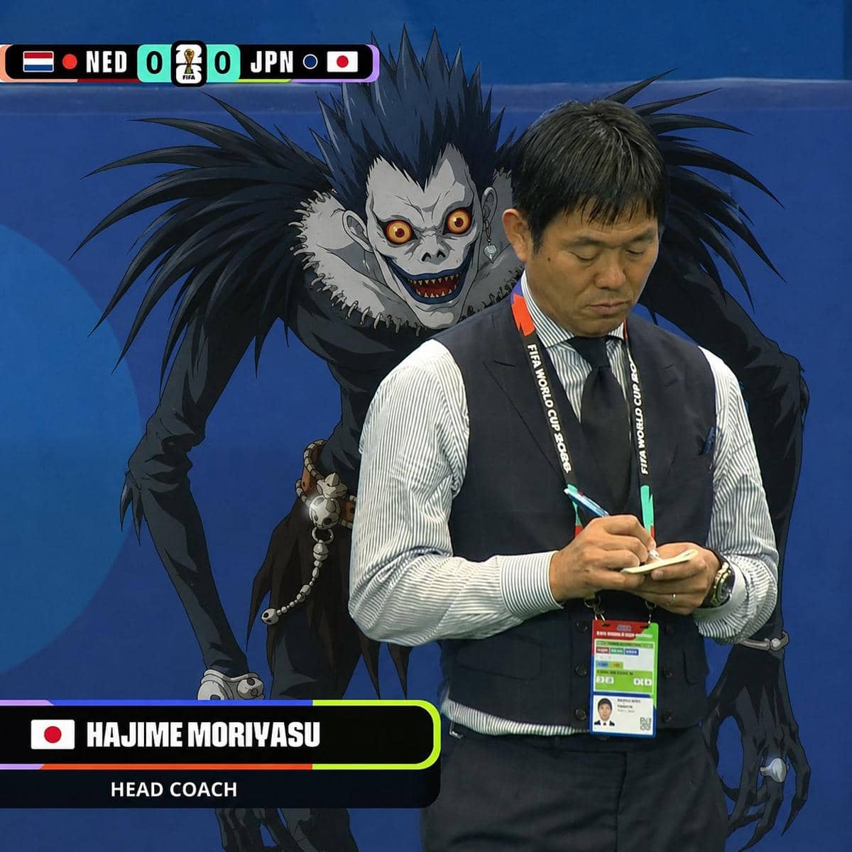 Pelatih tim nasional Jepang sedang menulis catatan di pinggir lapangan dengan karakter anime berwajah seram berdiri di belakangnya.