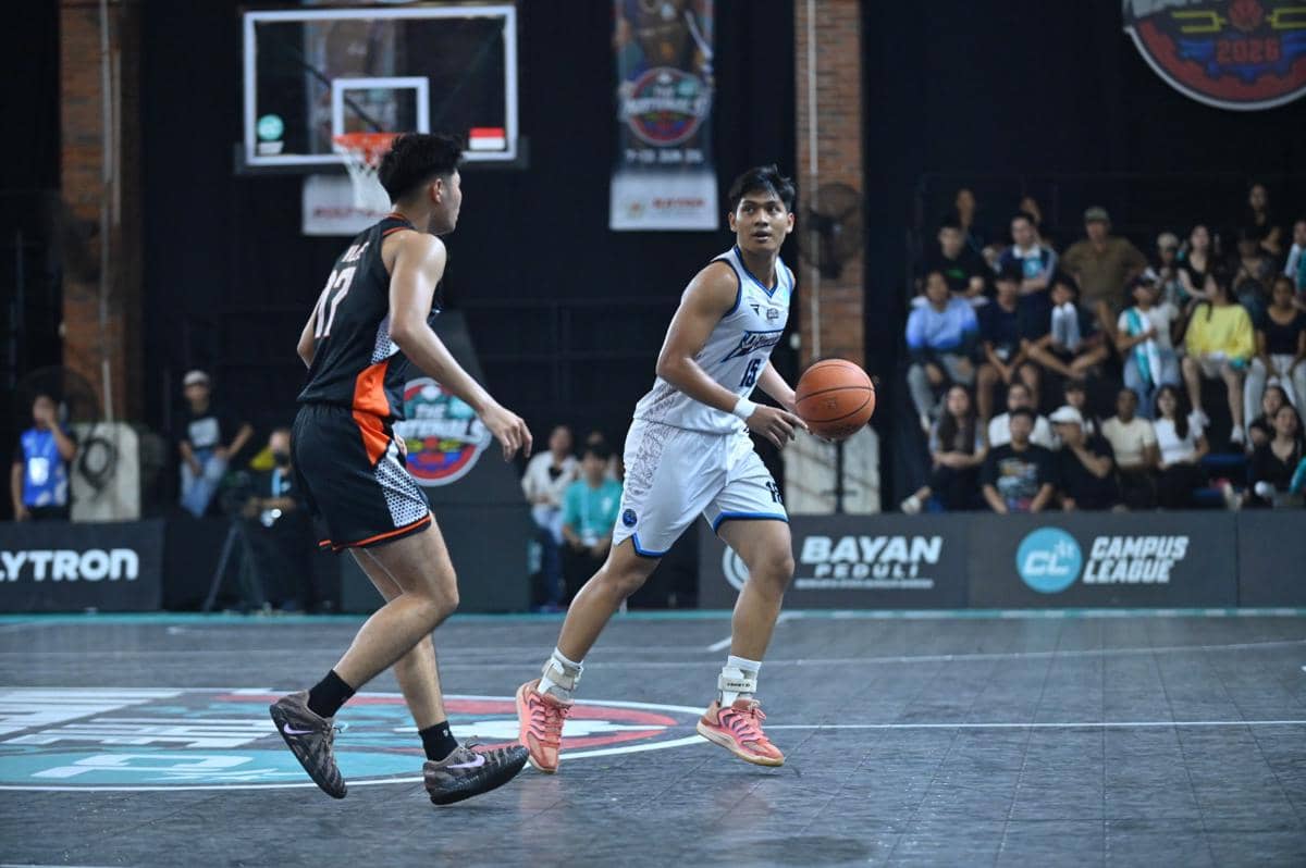 Pemain basket universitas mengenakan seragam putih menggiring bola menghadapi lawan berseragam hitam dalam pertandingan Campus League Basket 2026.